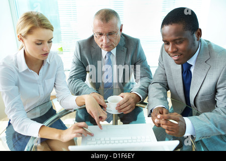 Pretty secretary by laptop explaining something to her boss and colleague Stock Photo
