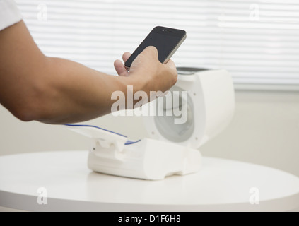 Hand holding a smartphone and an automated sphygmomanometer Stock Photo