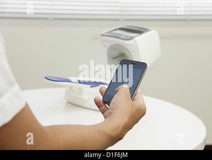 Hand holding a smartphone and an automated sphygmomanometer Stock Photo