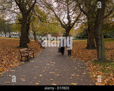 Man and Woman holding hands walking along a  leafy footpath in parkland with trees and fallen leaves Sheffield UK Stock Photo