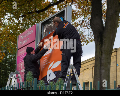 Two men putting up a new sign on a large billboard in Sheffield South Yorkshire England Stock Photo