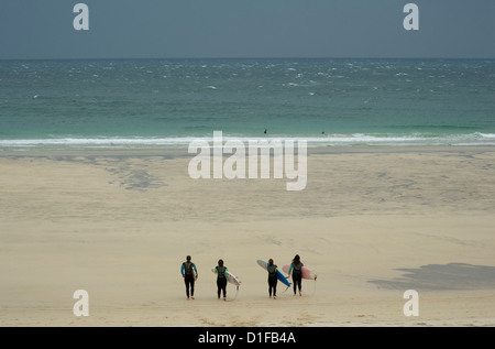 Four surfers in wet suits carrying boards and heading down the beach in St. Ives, Cornwall, England Stock Photo