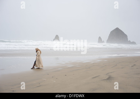 Woman talks on phone with Haystack Rock in the distance at popular tourist destination, Cannon Beach, Oregon, USA Stock Photo