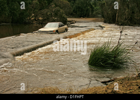 Car been driven through dangerously deep and fast flowing floodwaters of rivercrossing a road in Australia Stock Photo