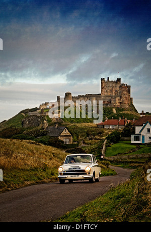 1965 Ford Lotus Cortina driving on the Northumberland coastal route with Bamburgh castle in the background. Stock Photo