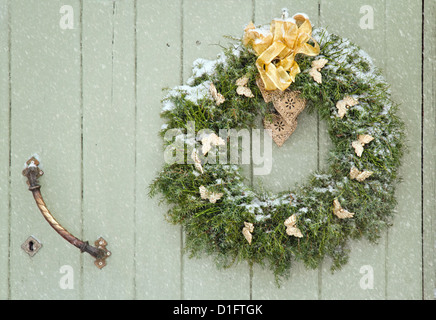 Green Christmas wreath in snowfall on a wooden green rustic door Stock Photo