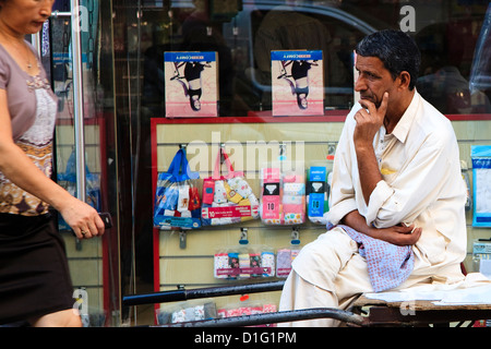 Arab man sitting on wheelbarrow in the Old Souk, Dubai watching an attractive woman walk by, and trying not to make it obvious Stock Photo