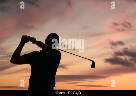 Golfer swinging a golf club silhouetted against a dusk sky, close up Stock Photo