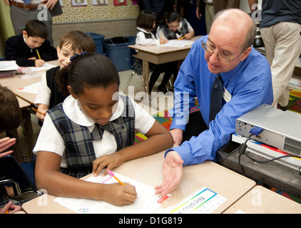 White male teacher assists African-American and Anglo students wearing uniform at private Catholic elementary school in Texas Stock Photo