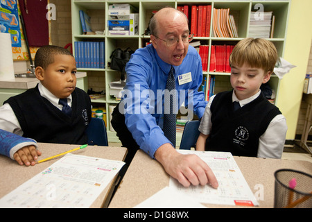 White male teacher assists African-American and Anglo students wearing uniform at private Catholic elementary school in Texas Stock Photo