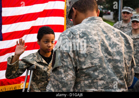 Khalil Quarles, 10, raises his right hand during his honorary enlistment into the Army Reserve as his father,  watches December 20, 2012 in Baltimore, MD. Khalil's dream is to be a soldier but suffers from a rare form of terminal cancer. Soldiers with the 200th Military Police Command showed up at Khalil's house and held a Enlistment Ceremony as well as providing a uniform, dogtags, a flag, and a ride in an armored Humvee. Stock Photo