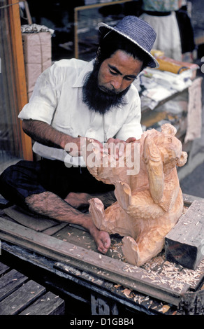 A bearded Ainu man carves a wood bear for sale in a village of indigenous Japanese people visited by tourists in 1962 on the island of Hokkaido, Japan. Stock Photo