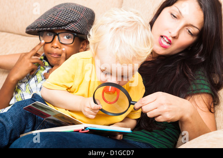 Young woman and children reading book with magnifying glass. Stock Photo