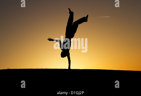 silhouetted boy doing one handed handstand in sunset Stock Photo