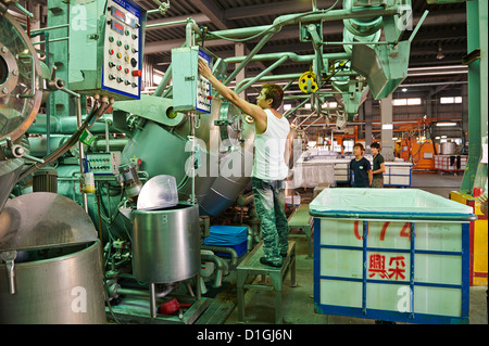 A strong worker poses and inspects fabric next to large dying machines at a textile manufacturer Stock Photo