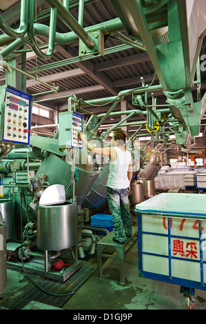 A strong worker poses and inspects fabric next to large dying machines at a textile manufacturer Stock Photo