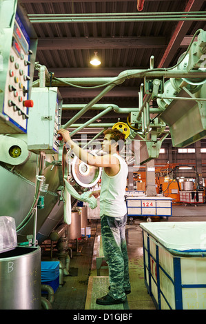 A strong worker poses and inspects fabric next to large dying machines at a textile manufacturer Stock Photo