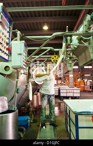 A strong worker poses and inspects fabric next to large dying machines at a textile manufacturer Stock Photo