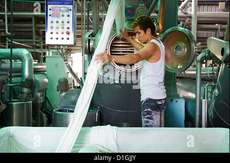 A strong worker poses and inspects fabric next to large dying machines at a textile manufacturer Stock Photo