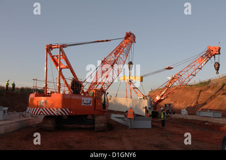Two large cranes  craning in  Bebo pre-cast concrete sectional arch bridge construction sections new road building site UK Stock Photo