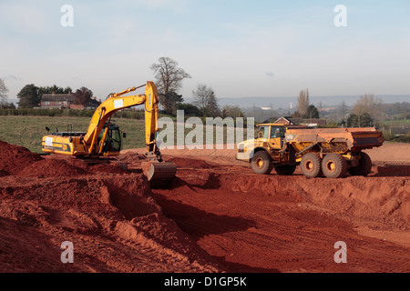 Tracked JCB backhoe excavator loading truck on highway construction building site UK Stock Photo