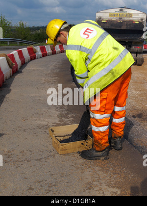 Road surfacing worker putting asphalt material into cardboard sample box for materials testing in the laboratory mat lab uk Stock Photo