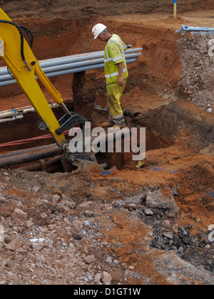 Excavator digging a trench watched by banksman underground services ...