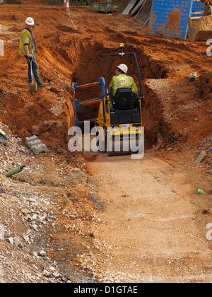 Small roller compacting compaction of fill soil backfilling trench road building construction site in the UK Stock Photo
