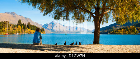 Panorama of a tourist relaxing by Lake Wakatipu in autumn at Queenstown, Otago, South Island, New Zealand, Pacific Stock Photo