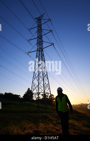 Silhouetted electricity pylons and worker in hard hat Stock Photo