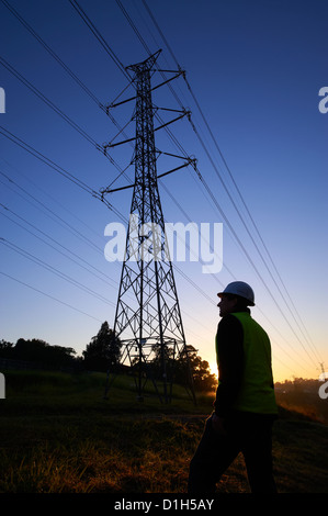 Silhouetted electricity pylons and worker in hard hat Stock Photo