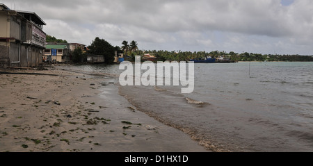 Grey cumulus clouds coastal view wet beach sand, sea, houses, Grenville, looking north to blue fishing boat moored pier, Grenada Stock Photo