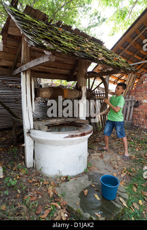 Schoolboy outdoor getting water from a vintage wooden well with pulley Stock Photo