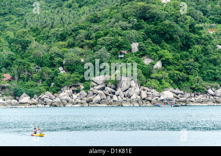 Couple paddling sea kayak in bay with large boulders on shore at Ko Tao in the Gulf of Thailand Stock Photo