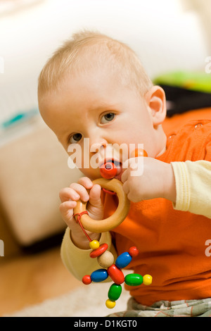 Baby boy sitting and playing - chewing a colorful wooden bead toy Stock Photo