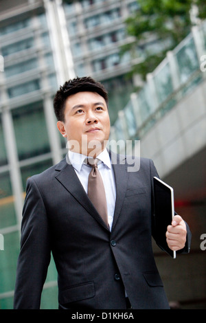 Confident mature businessman walking with digital tablet in hand, Hong Kong Stock Photo