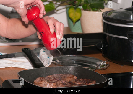 Person Adding Pepper Seasoning To A Fillet Steak Frying On A Griddle Pan Stock Photo