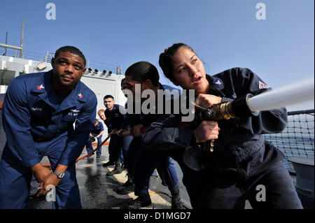 Sailors handle a fire hose as Gas Turbine System Technician (Mechanical) 1st Class Dain Swaby observes during damage control Olympics aboard the guided-missile destroyer USS Jason Dunham (DDG 109). Jason Dunham is deployed to the U.S. 5th Fleet area of responsibility conducting maritime security operations, theater security cooperation efforts and support missions for Operation Enduring Freedom.ARABIAN SEA (Dec.29, 2012) US Navy Photo Stock Photo