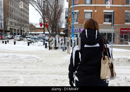 people waiting at snow covered intersection to cross city street Saskatoon Saskatchewan Canada Stock Photo