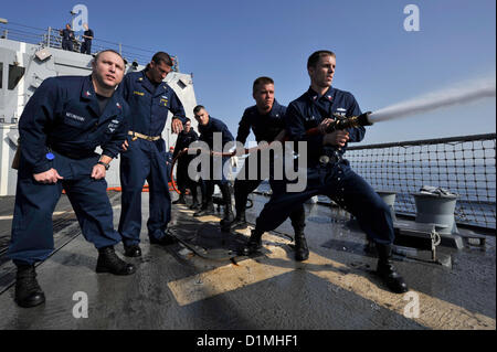 Sailors handle a fire hose as Hull Maintenance Technician 1st Class Kent Neumann, left, and Chief Boatswain’s Mate Aaron Stewart observe during damage control Olympics aboard the guided-missile destroyer USS Jason Dunham (DDG 109). Jason Dunham is deployed to the U.S. 5th Fleet area of responsibility conducting maritime security operations, theater security cooperation efforts and support missions for Operation Enduring Freedom. .ARABIAN SEA (Dec.29, 2012) US Navy Photo Stock Photo