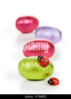 Chocolate candy Easter eggs wrapped in foil with two ladybugs on white Stock Photo