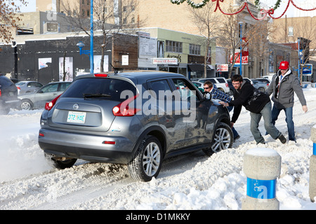 group of men pushing car stuck in deep snow on downtown city street Saskatoon Saskatchewan Canada Stock Photo