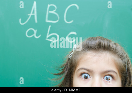 Scared Schoolgirl at Blackboard in classroom Stock Photo