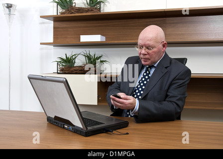A company director checking his mobile telephone, whilst using his laptop Stock Photo