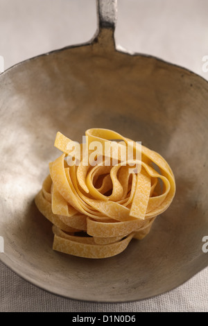 Raw fettuccine pasta in ladle Stock Photo