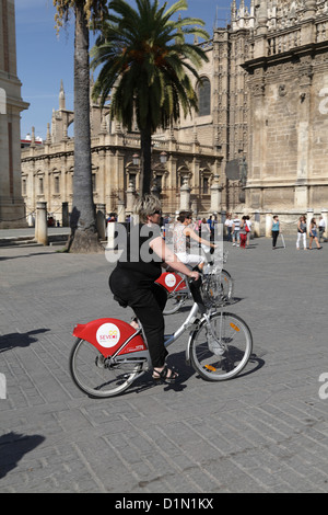 Two women riding hire Boris bikes in Seville near the cathedral Sevilla Spain sponsored by advertisement for Cruzcampo beer Stock Photo