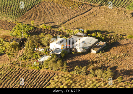 An aerial photograph captures a small rural farmstead nestled among terraced agricultural fields. The settlement consists of several modest structures with corrugated metal and mixed roofing Stock Photo