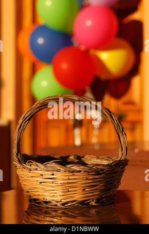 A wicker basket in front of a door with balloons in out of focus. Stock Photo