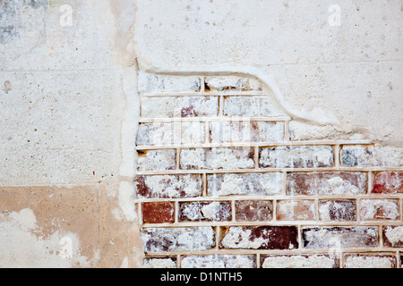 Brick wall with plaster on top, and the plaster is cracked and breaking off revealing the red brick underneath Stock Photo