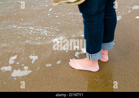 Woman standing barefoot in water on the beach holding her shoes. Ocean Beach, San Francisco, California. Stock Photo